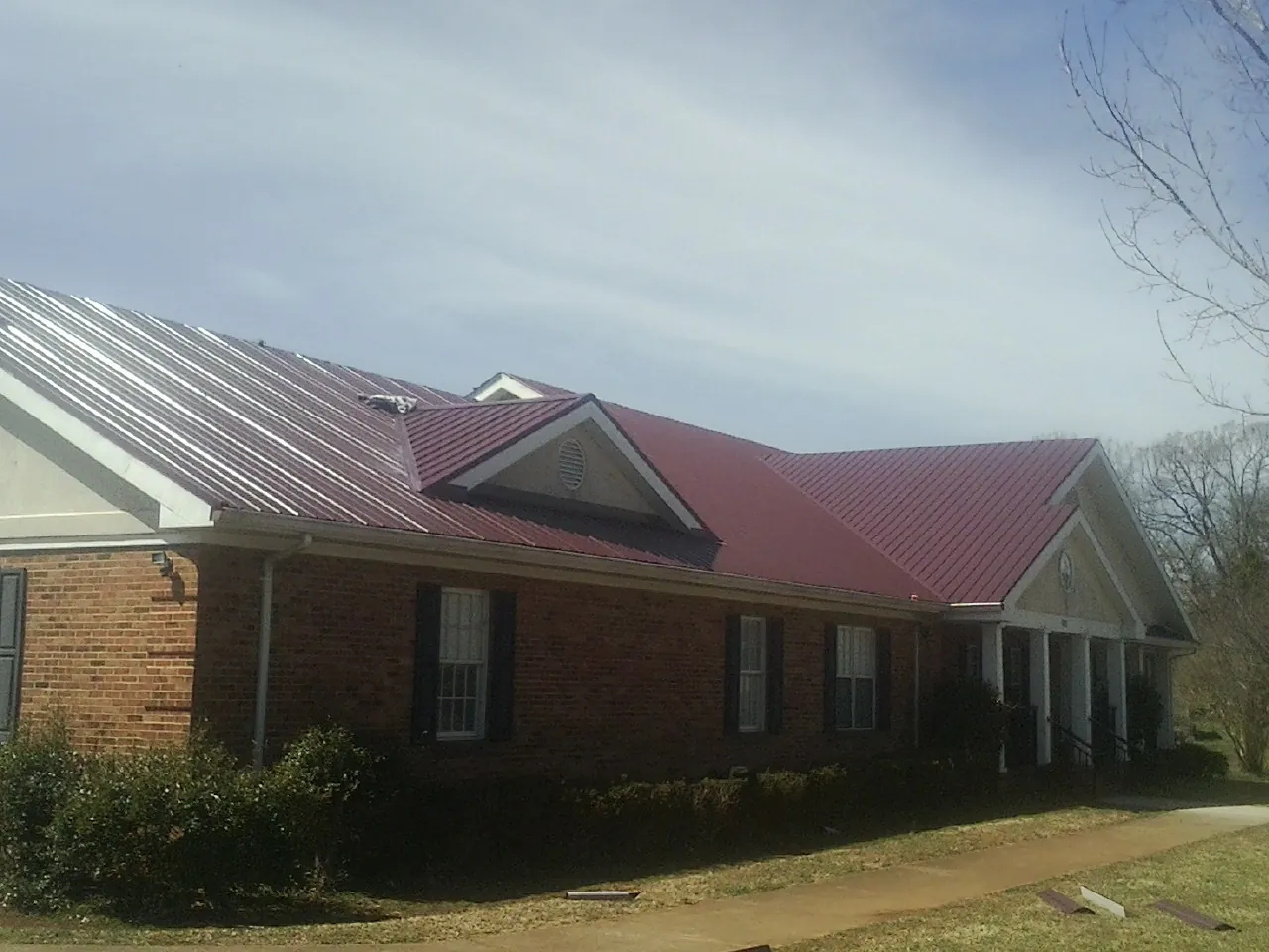 Red metal roof with gabled entries on a long brick building, from a Hail Damage Roof Repair job in Saugus