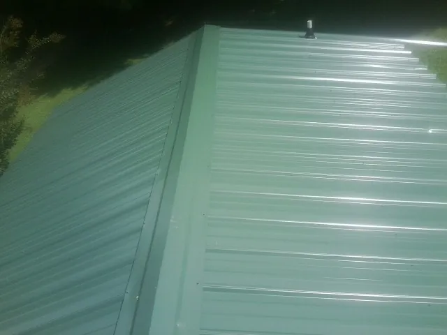 New green metal panels meeting at the ridge of a roof — Flat Roof Repair work by our crew in Saugus