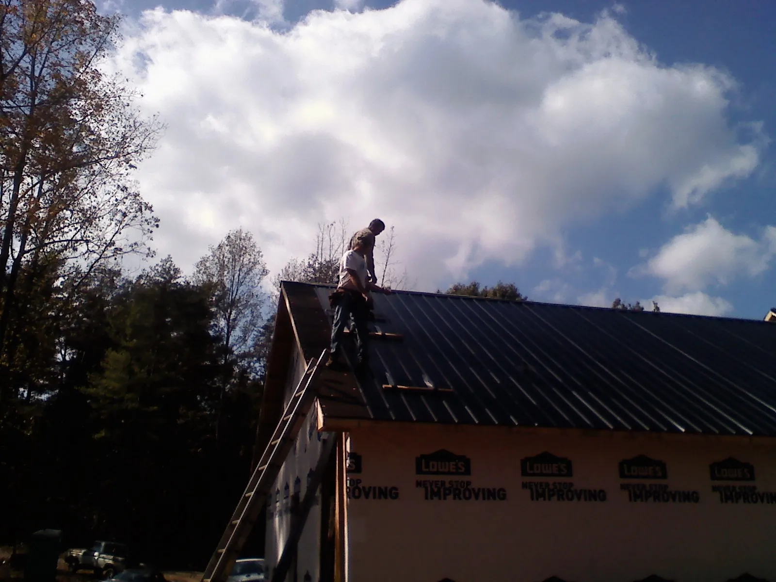 Roofer fastening dark metal panels high against a cloudy sky, from a Roof Inspection job in Saugus