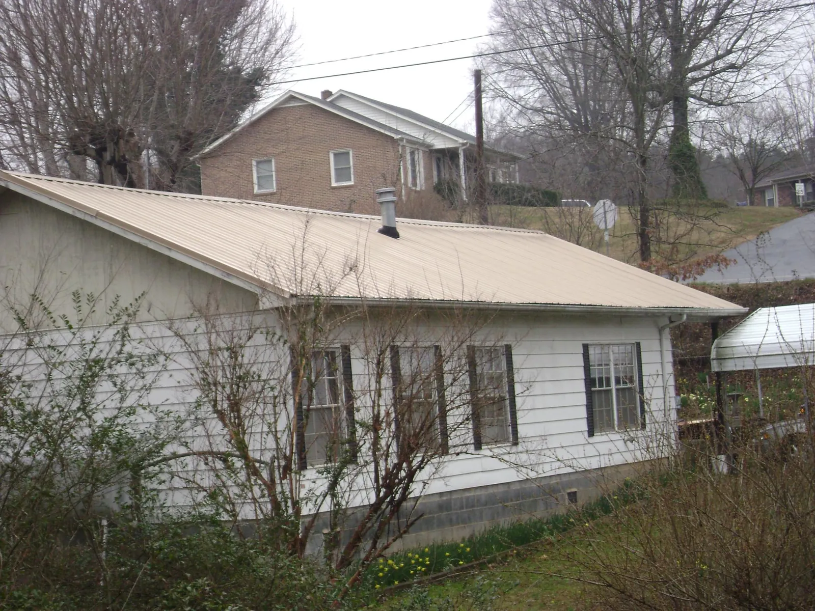 Tan metal roof on a white sided house set into a hillside — Commercial Roofing by Roofing Brothers in Saugus